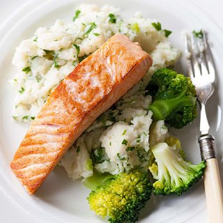 A fillet of fried salmon served on mashed potato mixed with spring onion and 3 florets of broccoli.