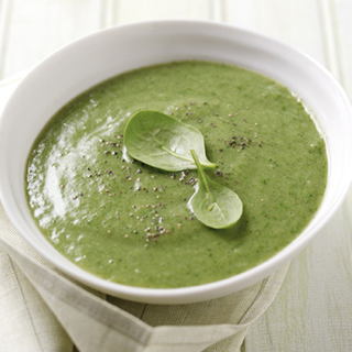 A portion of super veggie soup, served in a bowl and garnished with 2 spinach leaves.